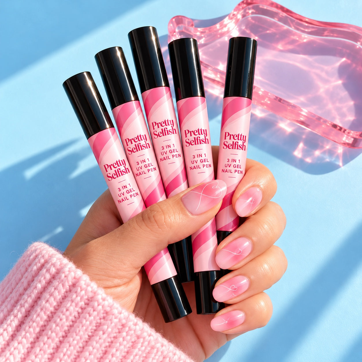 Hand holding five branded Pretty Selfish gel nail pens on a blue background